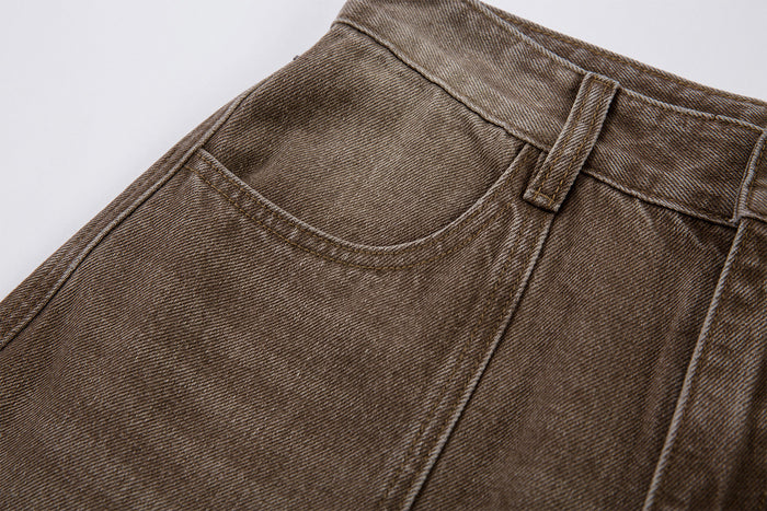 Close-up of the brown denim waistband, belt loop, curved front pocket opening, and visible weave texture