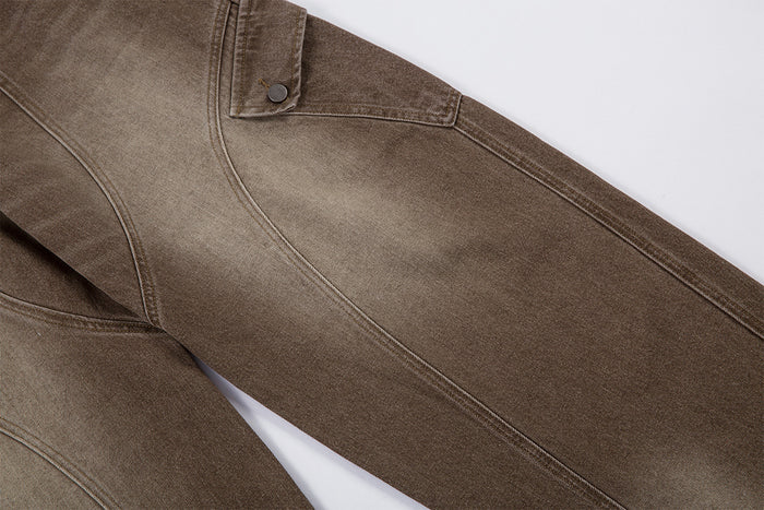Close-up of a brown cargo jean leg showing curved seam detailing, washed shading, and a buttoned pocket flap