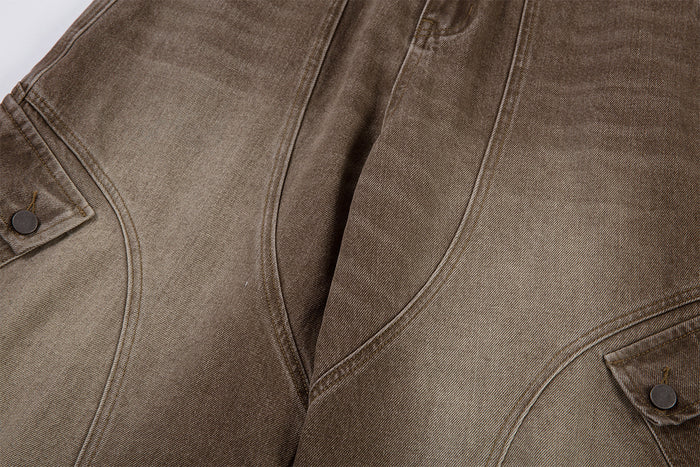 Front thigh close-up highlighting the curved panel seams and buttoned cargo pocket flaps on brown washed denim
