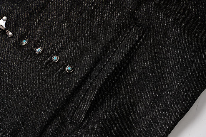 Close-up of black denim jacket fabric with a vertical welt pocket seam and turquoise stud accents