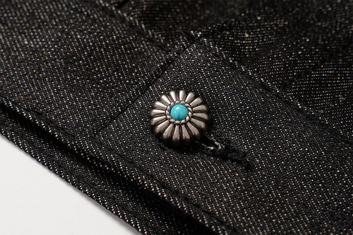 Close-up of a turquoise-centered silver-toned decorative stud set against black denim fabric