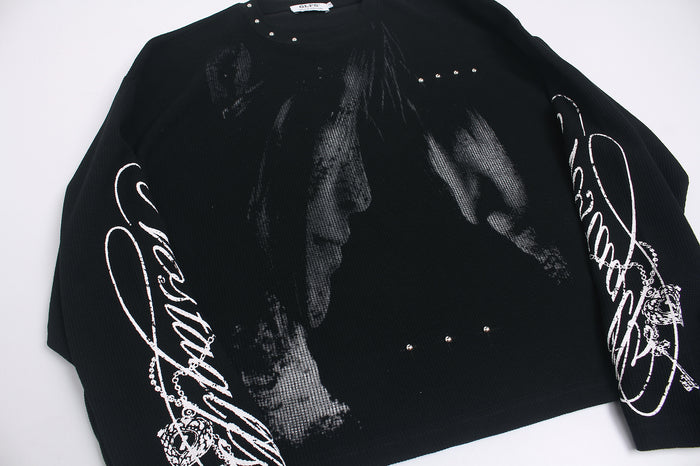 Angled close view of a black graphic tee with gray front artwork, white sleeve script, and small metallic studs
