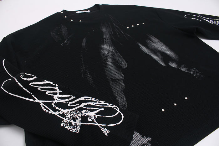 Close angled view of the black tee front showing textured gray artwork, sleeve script, and scattered stud details