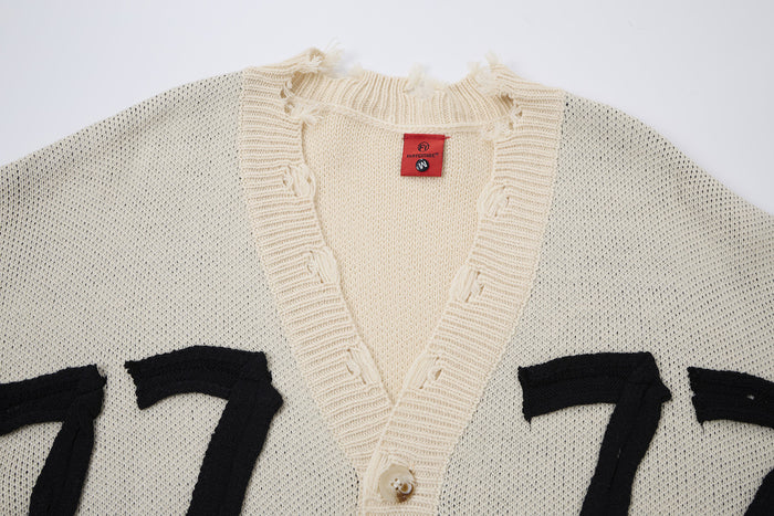 Close-up of the cream cardigan neckline, ribbed button placket, knit texture, and black 77 graphics