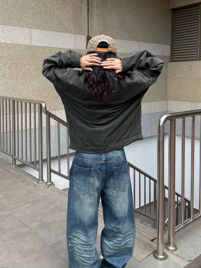 Rear view of a model adjusting a dark army green jacket, showing the relaxed back and distressed finish