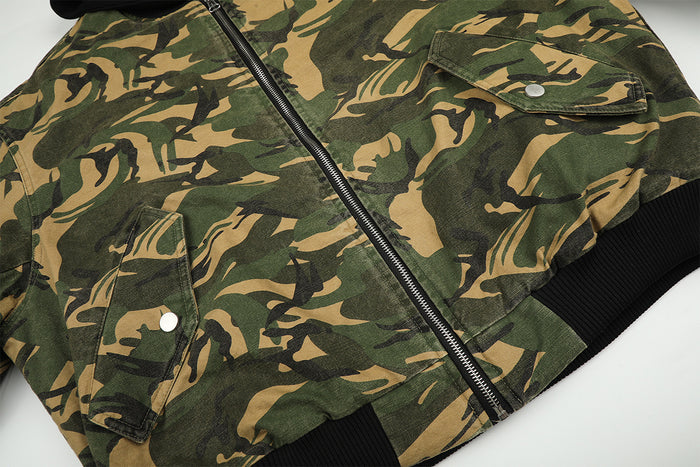 Close-up of the camouflage jacket front showing the metal zipper, flap pockets, snap fasteners, and black ribbed hem