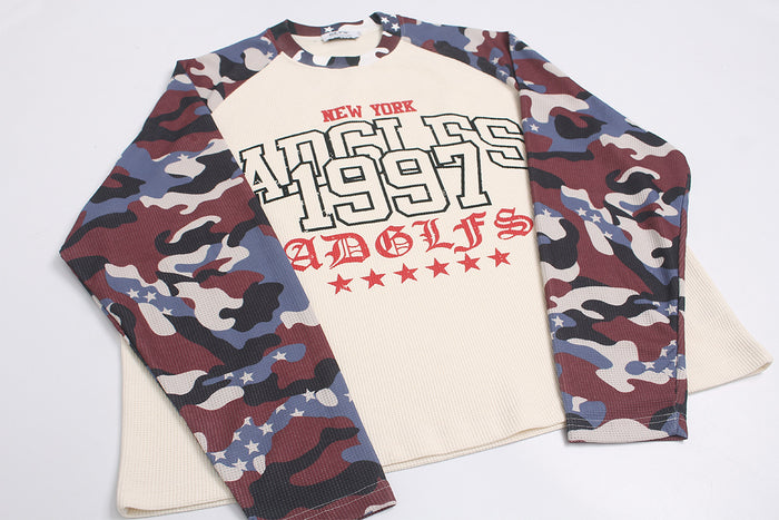 Angled flat lay of a cream waffle-knit raglan shirt with multicolor camouflage sleeves and New York 1997 graphic