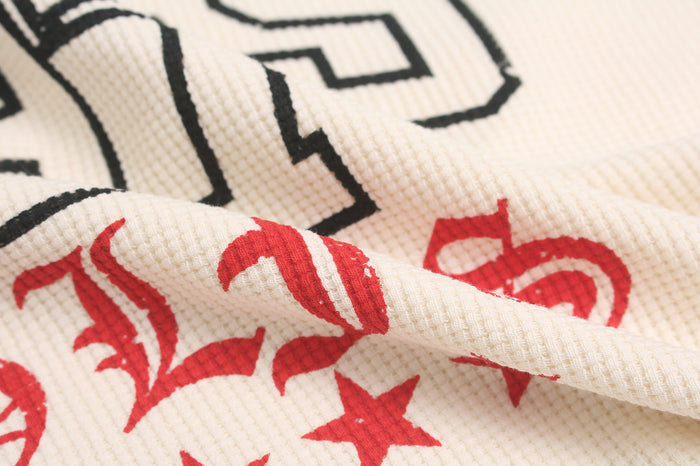Close-up of raised cream waffle-knit texture with folded fabric and partial black and red graphic