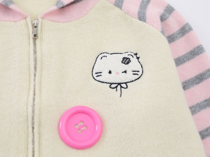 Close-up of the cream knit hoodie front showing an embroidered cat face and large pink button beside the zipper