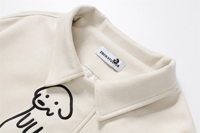 Close-up of the cream jacket collar, label, and black cartoon dog embroidery on the upper front