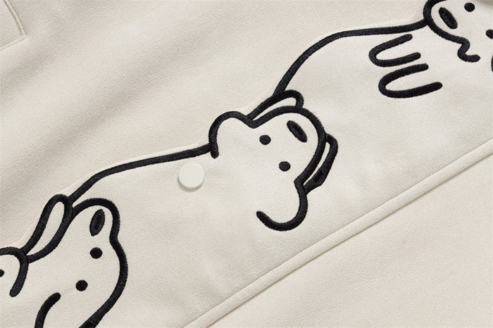 Close-up of black cartoon dog embroidery beside a white snap button on the cream jacket front