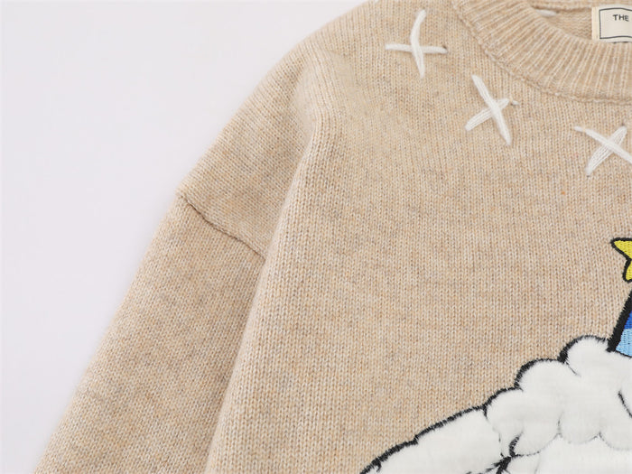 Close-up of the beige knit sweater shoulder and sleeve with white X stitching and part of the sheep design