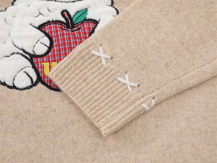 Close-up of the beige ribbed sleeve cuff with white X stitching beside the sheep and apple graphic