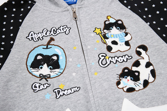 Close-up of gray hoodie front featuring embroidered cat illustrations, stars, text, and a center zipper