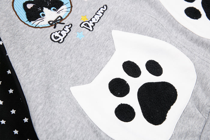 Close-up of a white cat-shaped paw pocket with black paw-print appliqué on the gray hoodie front