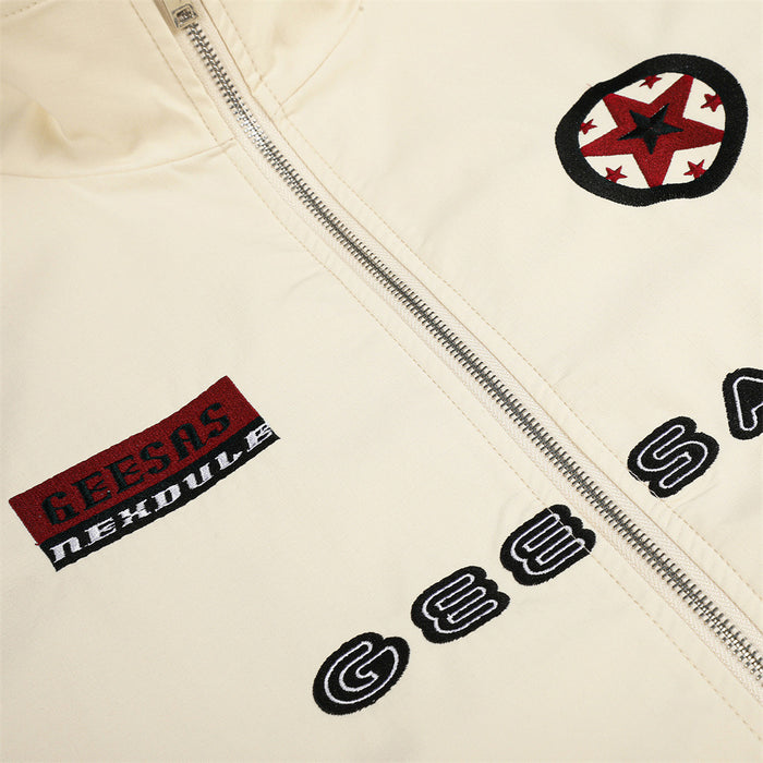 Cream jacket close-up showing the silver zipper, circular star patch, rectangular patch, and embroidered chest lettering