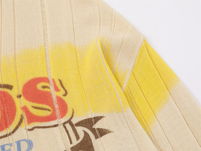 Close-up of the cream sweater shoulder and sleeve with vertical ribbing, yellow stripe, and graphic detail