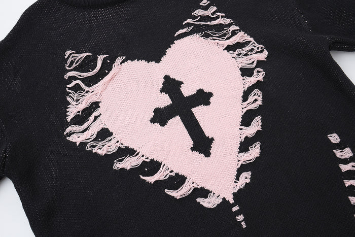 Close-up of a pale pink distressed heart and black cross graphic on a black knitted sweater
