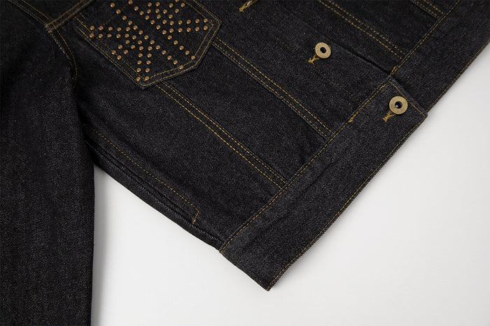 Close-up of the dark denim jacket front hem, gold stitching, button fastening, and studded pocket detail