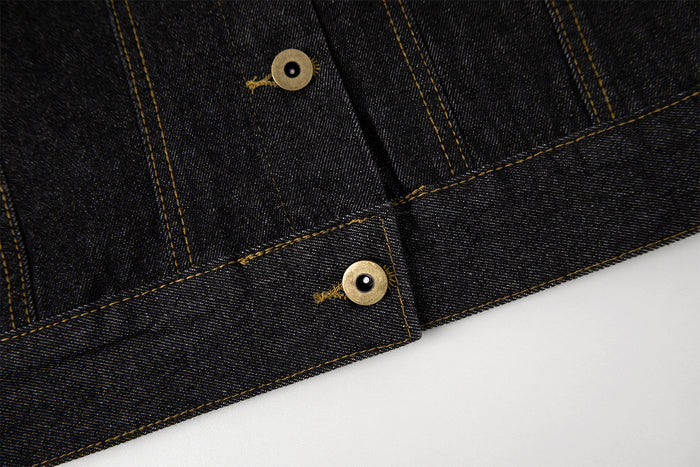 Close-up of the dark denim jacket lower front showing gold buttons, stitched panels, and the waistband