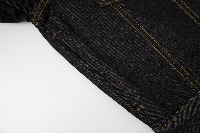 Close-up of dark denim jacket side seam and lower body, highlighting the textured denim and gold stitching