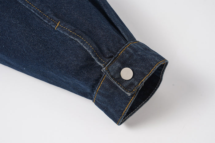 Close-up of the dark indigo denim jacket sleeve cuff with snap closure and yellow contrast stitching