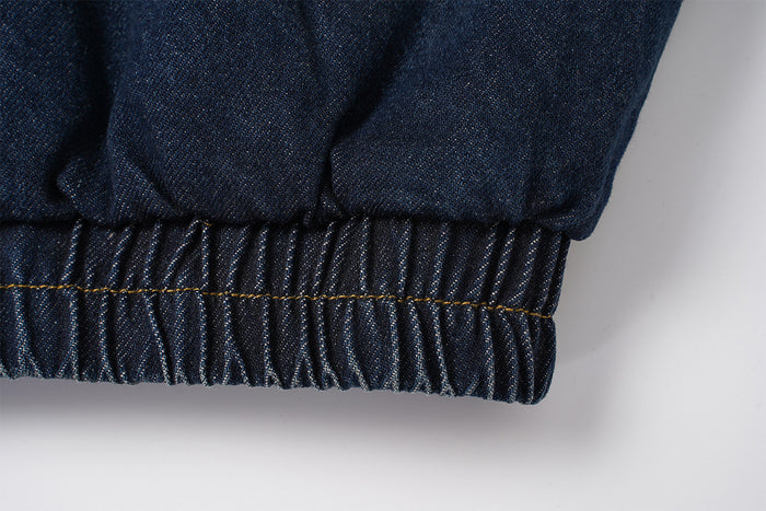 Close-up of the gathered elastic waistband on the dark indigo denim bomber jacket