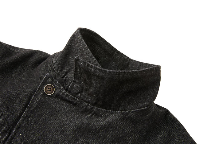 Close-up of the black denim jacket stand collar with topstitching and a visible button at the asymmetric closure