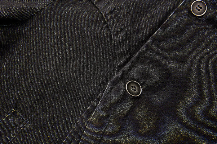 Close-up of black denim fabric showing the diagonal front closure, stitching and a dark button