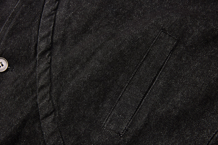 Close-up of the black denim front panel showing a stitched angled seam and partial button closure