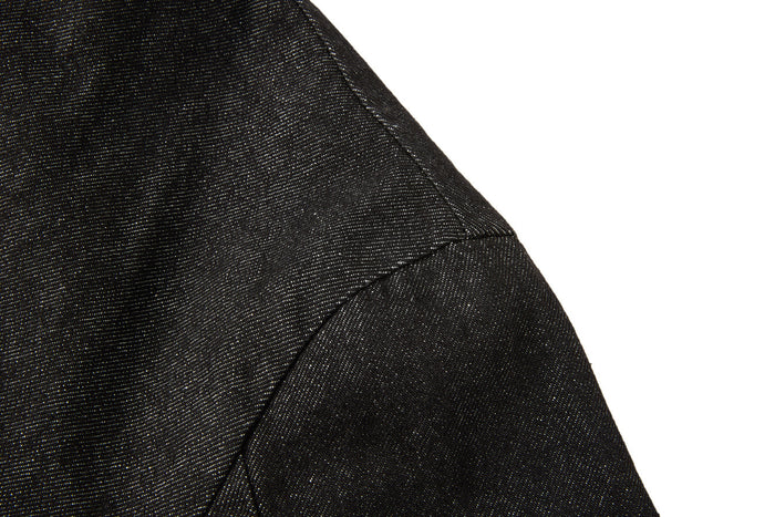 Close-up of the black denim jacket shoulder showing curved panel stitching and the sleeve seam