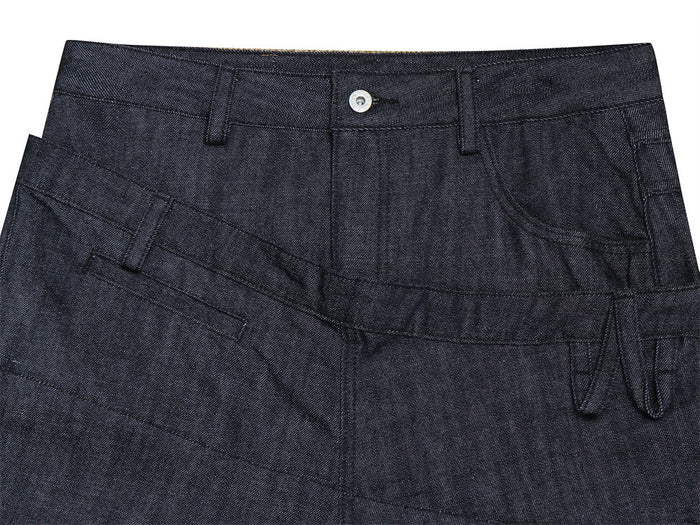 Close-up of the jeans front waistband showing the button, belt loops, diagonal seam, and layered pocket panel