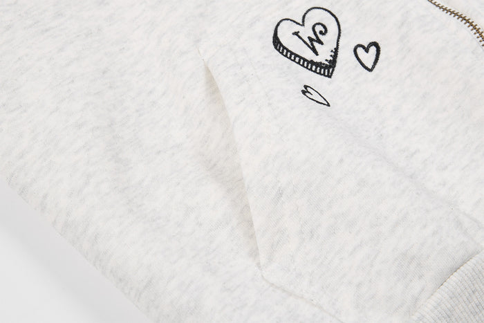 Light gray hoodie fabric close-up featuring black heart embroidery and a soft brushed texture