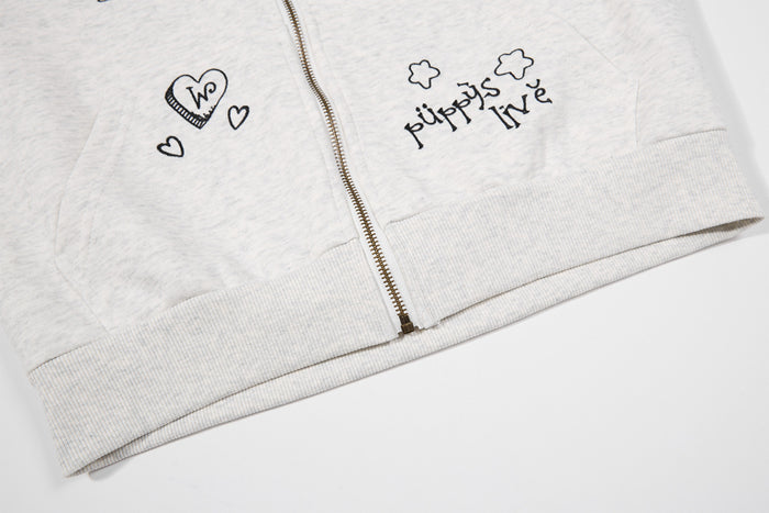 Lower front of the light gray hoodie showing the metal zipper, ribbed hem, pocket seam, and small graphic embroidery