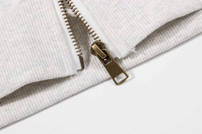 Close-up of the gold-tone metal zipper pull and teeth on the ribbed hem of the light gray hoodie