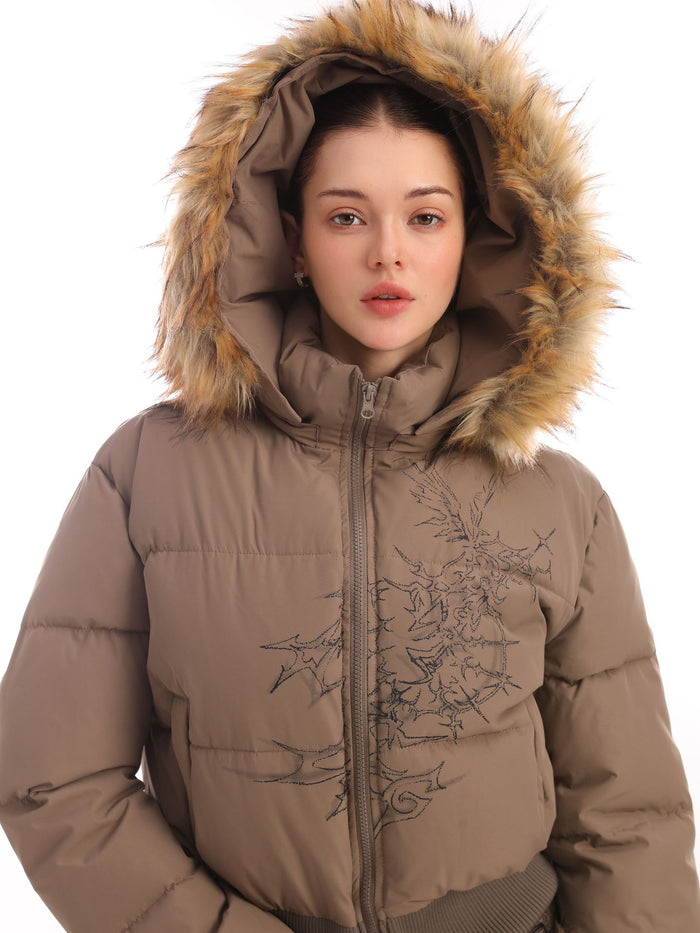 Close model view of a taupe hooded puffer jacket with fur trim and black thorn embroidery
