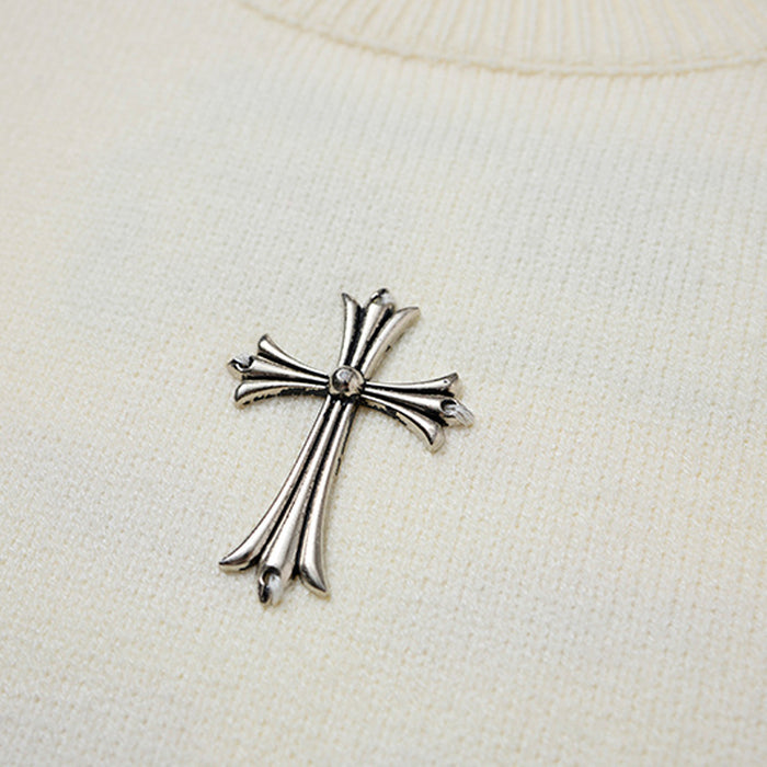 Close-up of a silver cross embellishment on the cream knitted sweater chest