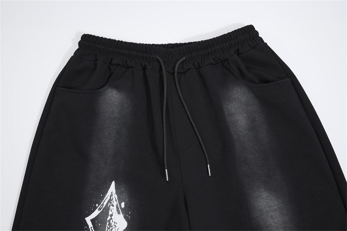 Close-up of black sweatpants showing the elastic drawstring waistband, side pockets, gray shading, and partial cross graphic