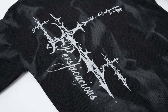 Close-up of the black sweater’s white thorny cross graphic printed across the marbled knit front
