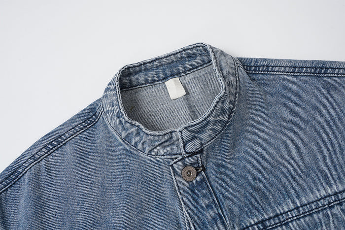 Close-up of the washed blue denim jacket's stand collar, top button, and textured stitched seams