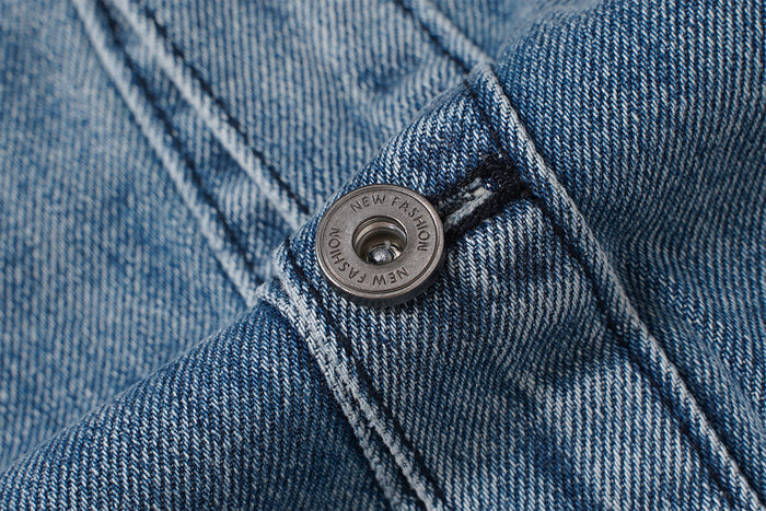 Close-up of a metal button secured on textured blue denim with contrasting stitched seams