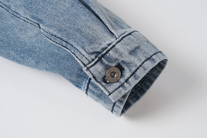 Close-up of the washed denim jacket sleeve cuff with button closure and reinforced stitching