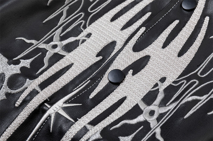 Detailed close-up of white abstract chest embroidery, black snaps and contrast stitching on a black PU jacket