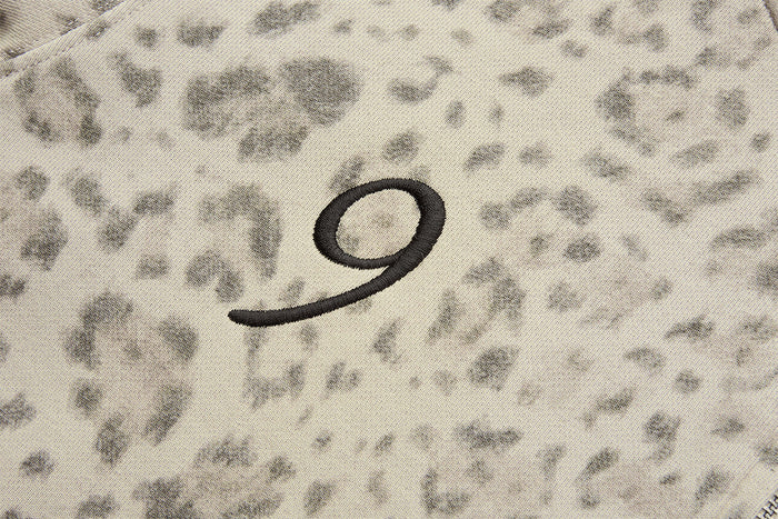 Close-up of a small black curved embroidered graphic on beige leopard-print hoodie fabric