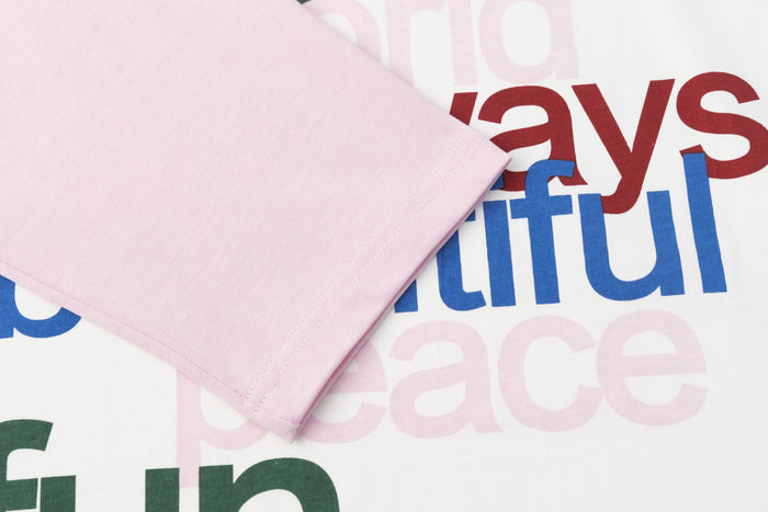 Close-up of a pale pink sleeve overlapping the multicolor text graphic on the white shirt front