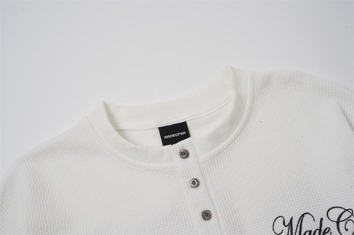 Close-up of the white henley collar, textured fabric, decorative buttons, and partial chest script
