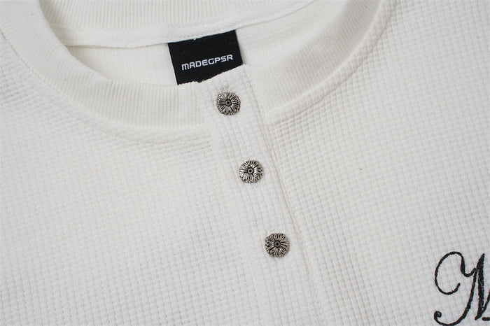 Close-up of three decorative metal buttons on the white textured henley placket