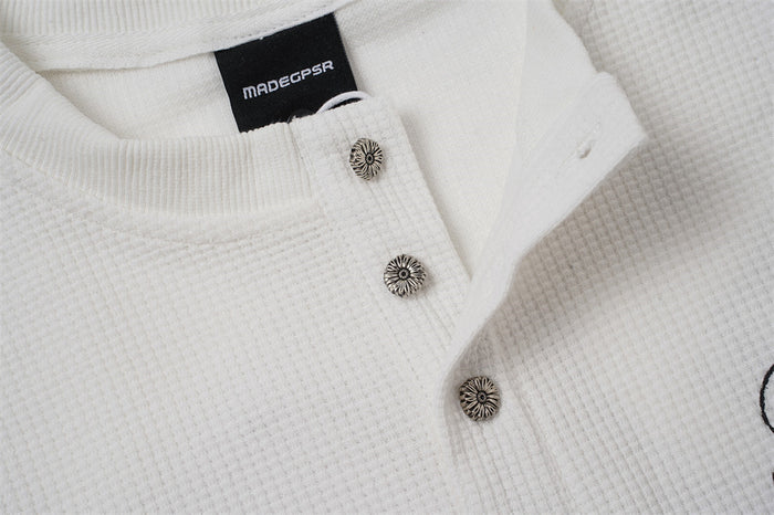 White henley placket shown partly open with three decorative buttons and textured fabric
