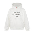 Front view of a white oversized pullover hoodie with rhinestone splatter, kangaroo pocket, and 1976 chest print