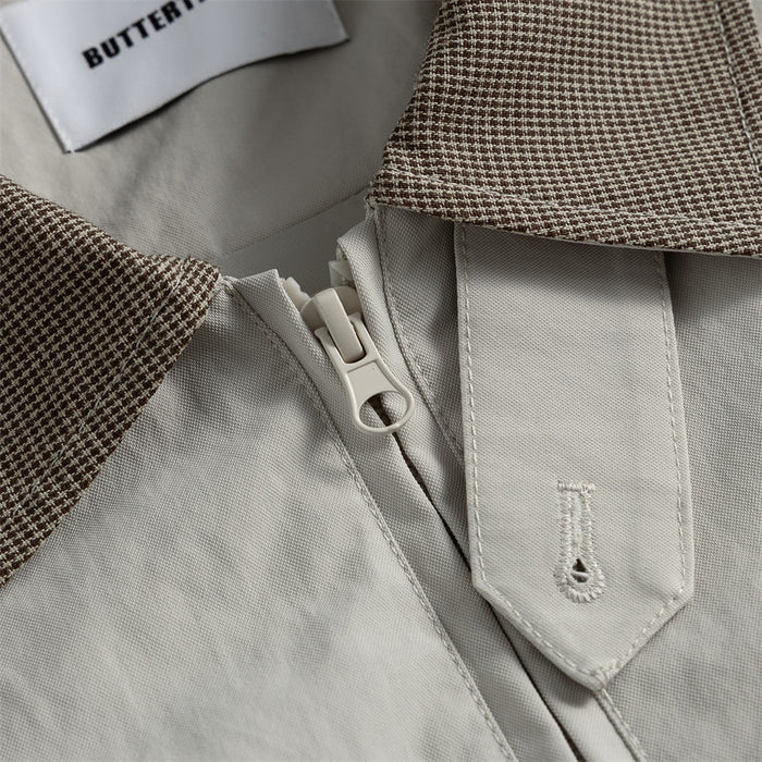 Detailed view of the houndstooth collar, zipper, and snap-fastened storm flap on the light gray jacket